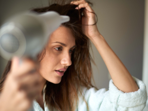 Erros que danificam diariamente seu cabelo. Foto mostra uma mulher branca secando o cabelo com secador