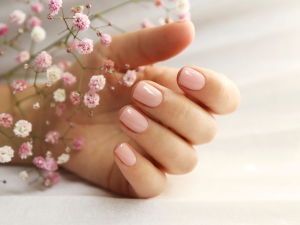 unhas curtas delicadas. Foto mostra mão sobre flores e com a unha pintada de nude