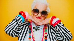 mulher idosa com roupa listrada e várias joias coloridas